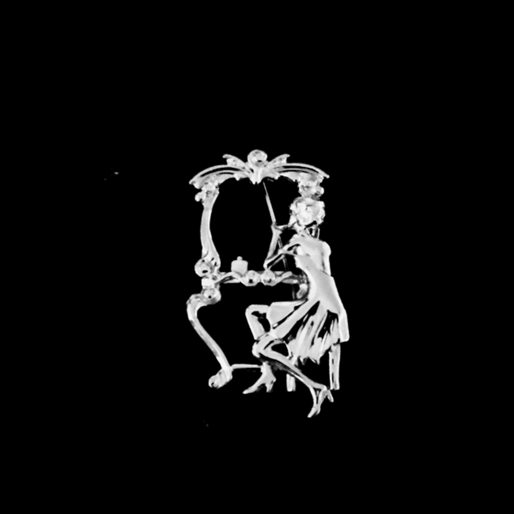 Silvertone brooch of lady looking in her mirror